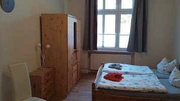 Une chambre à coucher avec un lit en bois, une chaise, une armoire et une fenêtre avec des rideaux.