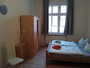 A bedroom with a wooden bed, a chair, a wardrobe, and a window with curtains. - Apartment "Villa Adler - Seeseite" with Sea View and Terrace (Seebad Ahlbeck)