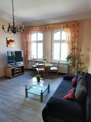 Un salon comprenant un canapé, une table basse en verre, un téléviseur et un coin repas avec des chaises et une table.