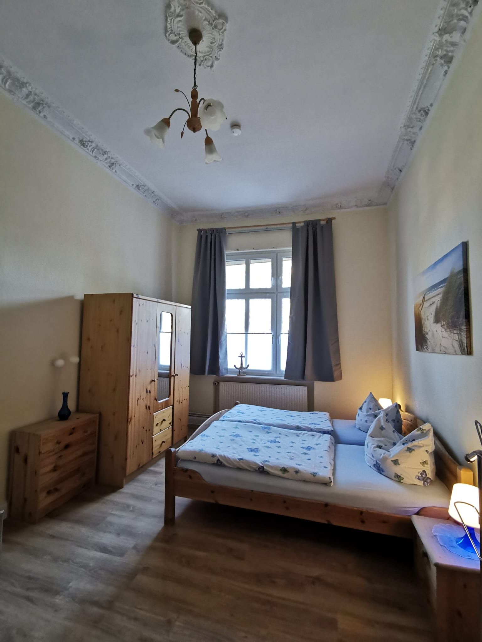 Ein Schlafzimmer mit einem hölzernen Bett, einem Schrank aus Holz, einem Fenster mit Vorhängen und einem Gemälde an der Wand.
