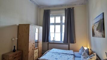 A bedroom with a wooden bed, a wooden wardrobe, a window with curtains, and a painting on the wall.
