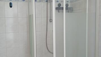 Eine begehbare Dusche mit Glaswänden, einer Handbrause und einem am Wand montierten Wasserhahn.