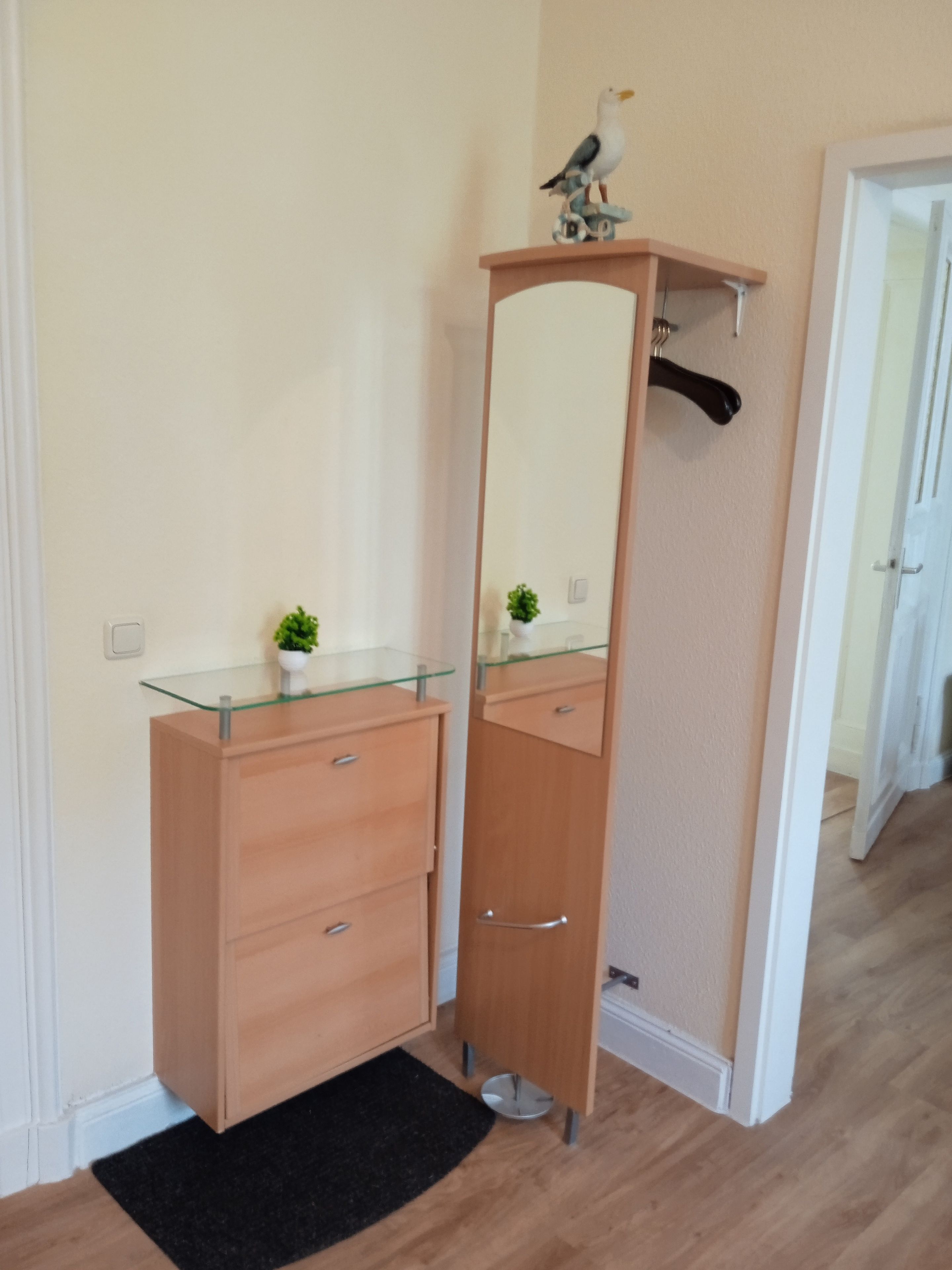 Et badeværelse med et trækommode, en glashylde, et spejl og en lille potteplante.