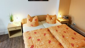 A bedroom with a bed, two pillows, a bedside table, a lamp, a wall-mounted picture, and a small plant. - Apartment "Villa Adler - Waldseite" (Seebad Ahlbeck)