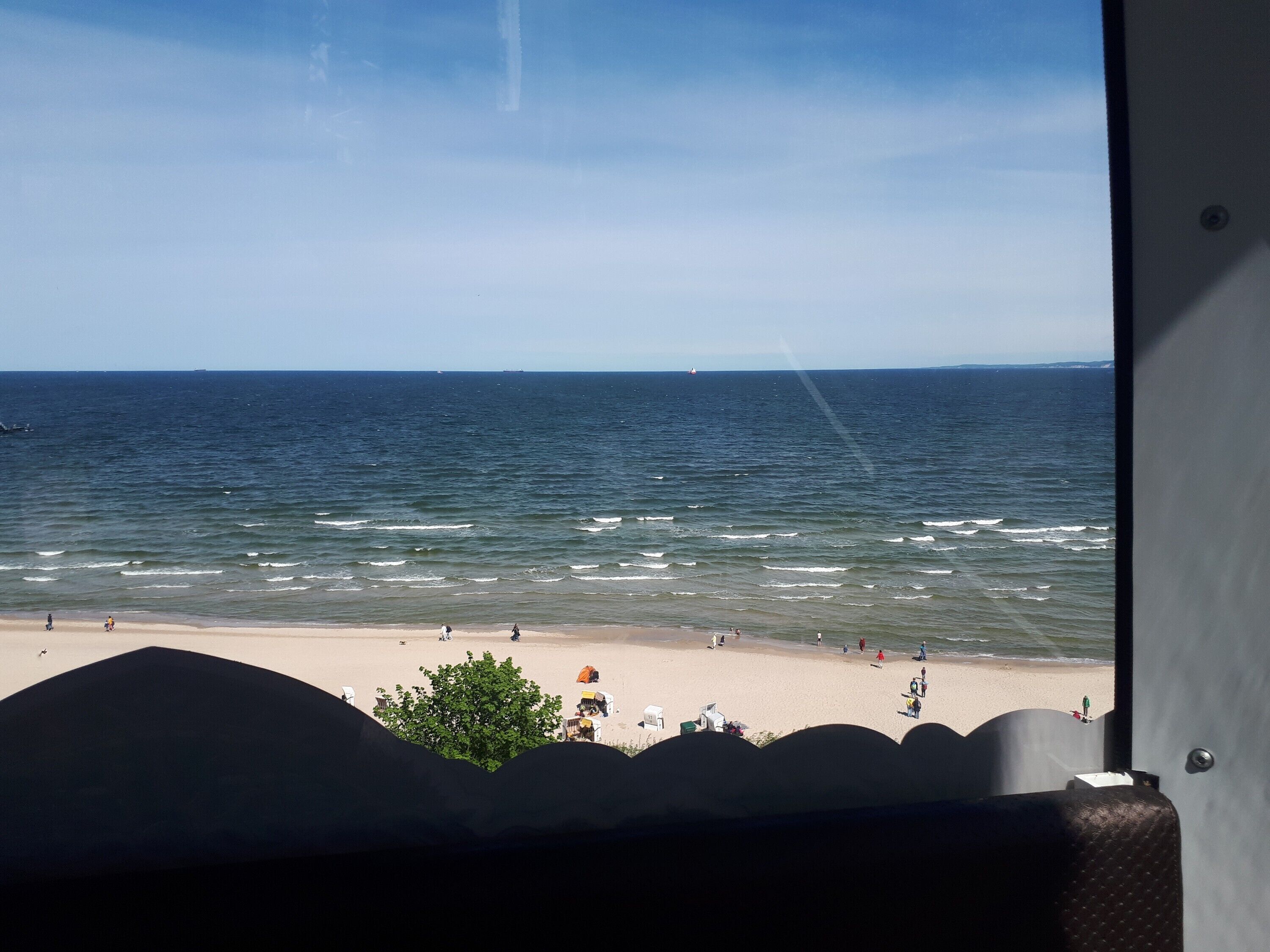 A view of the ocean from a window overlooking a beach with people and beach chairs.