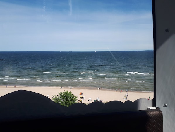 En utsikt över havet från ett fönster med utsikt över en strand där människor och strandstolar syns.