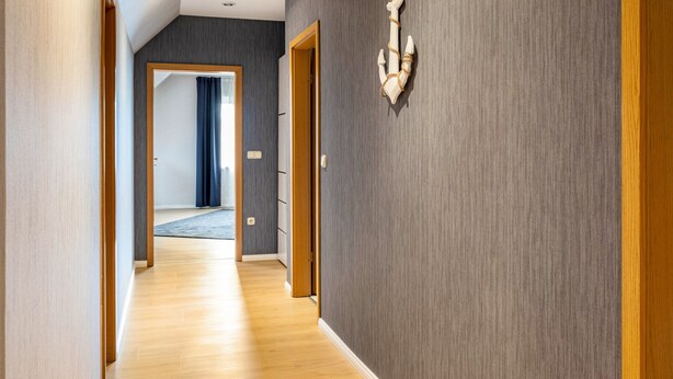 Um corredor com piso de madeira, parede escura texturizada e um objeto decorativo na parede.