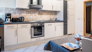 Cozinha moderna com armários brancos, forno embutido, máquina de café e área de jantar com mesa posta para dois.