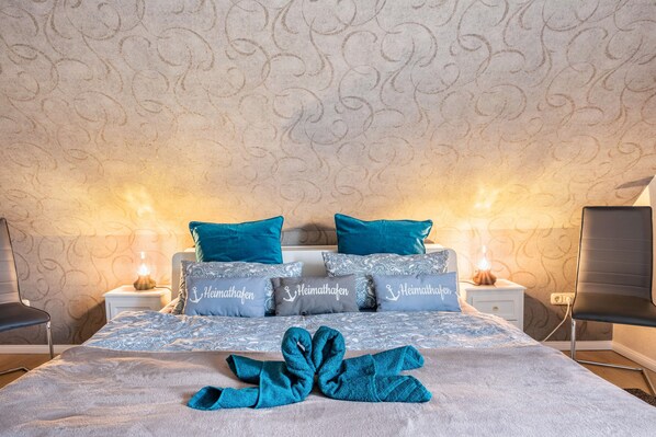 A neatly made bed with a blue towel, matching pillows, and a patterned wall.
