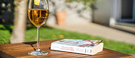A glass of amber liquid with a lemon peel garnish on a wooden table, next to a book titled 'Schwarzwälder Kirschmorde'.