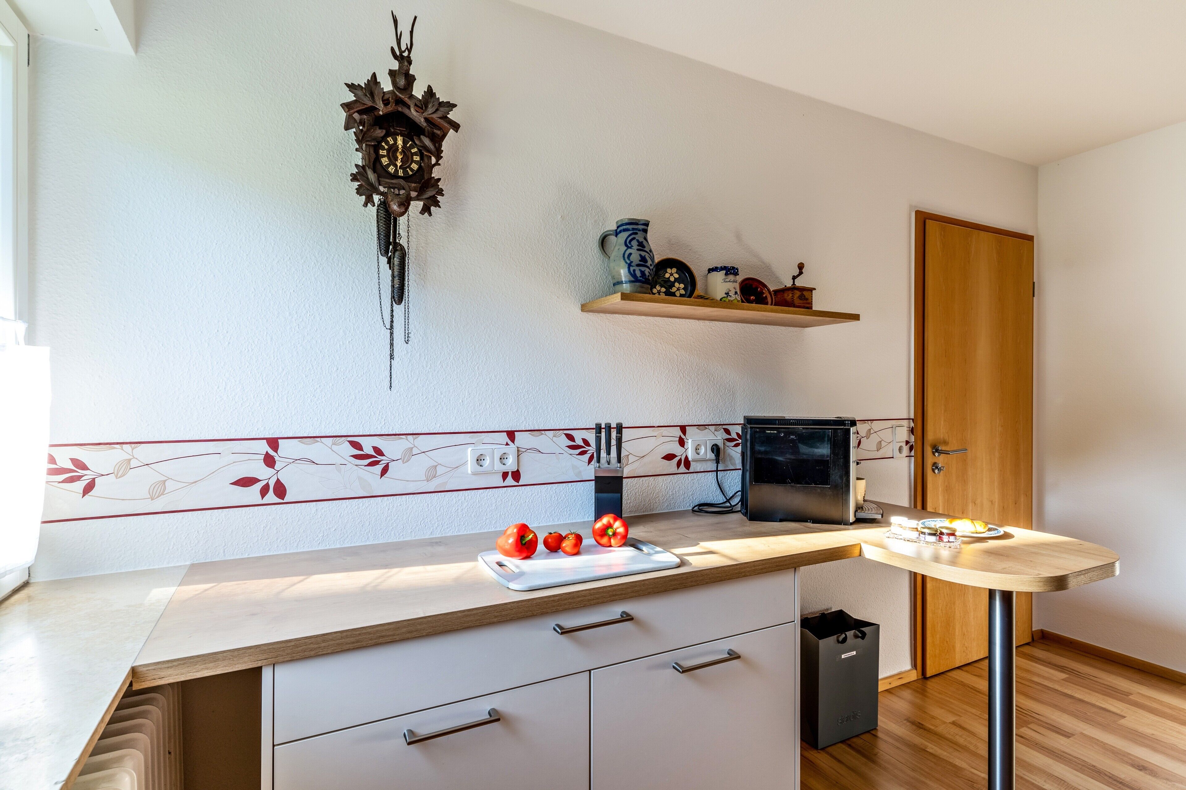 A kitchen with a wooden countertop, a wall-mounted clock, a microwave, and a door.