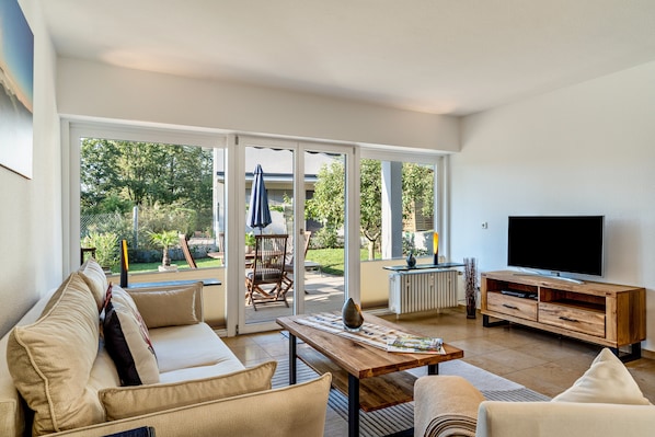 A living room with a sofa, coffee table, TV stand, and sliding glass doors leading to a patio with outdoor furniture.