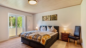 Ein Schlafzimmer mit Bett, Nachttisch, Sessel, Fenster und Tür.