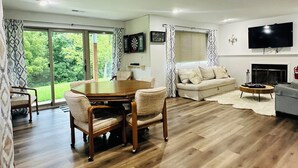 A spacious living room with a wooden floor, a dining area with a table and chairs, a sofa, a TV mounted on the wall, and a fireplace. - Galena 4BR • 4 Private Baths • Sleeps 10 • Game Room • Owners’ Club (Galena)
