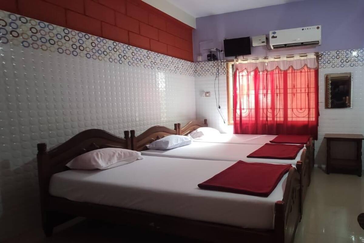 A hotel room with two beds, a small table, and an air conditioning unit on the wall.