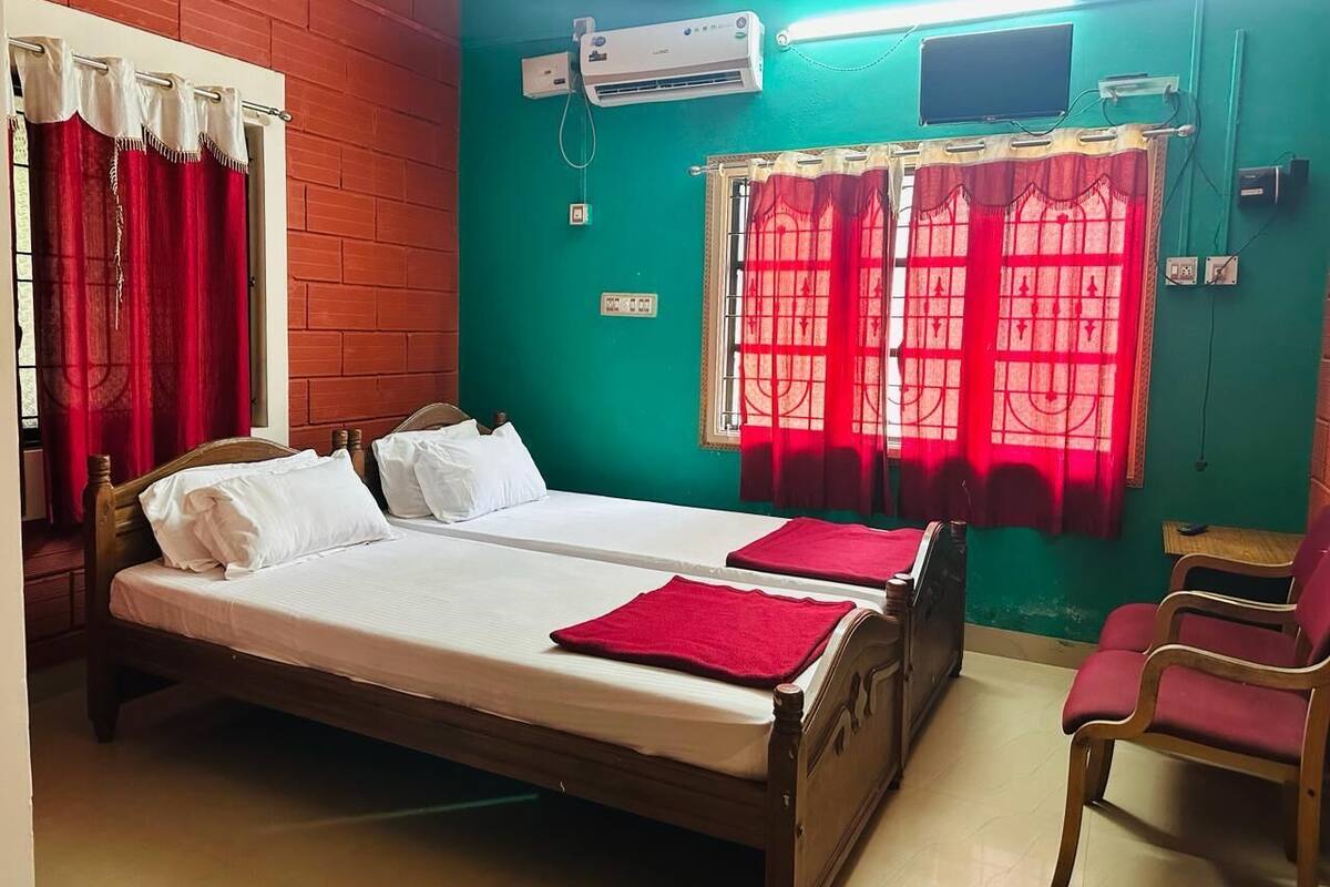 A room with two beds, red curtains, a TV, and a red chair.