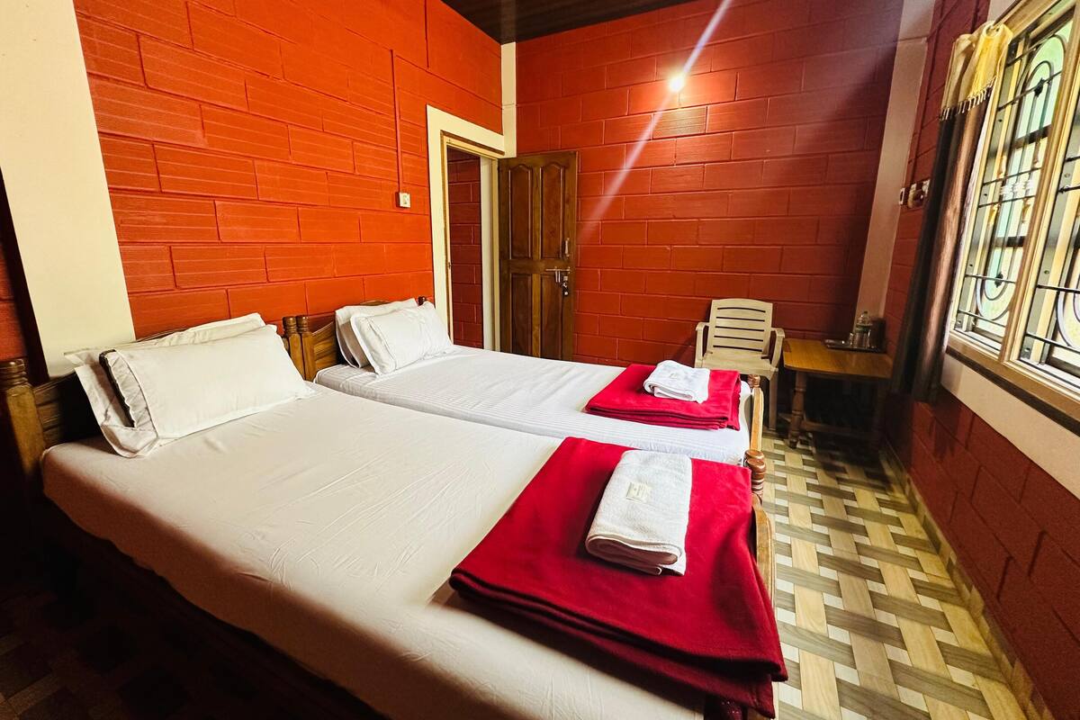 A hotel room with two beds, a wooden door, a small table, and a window with bars.