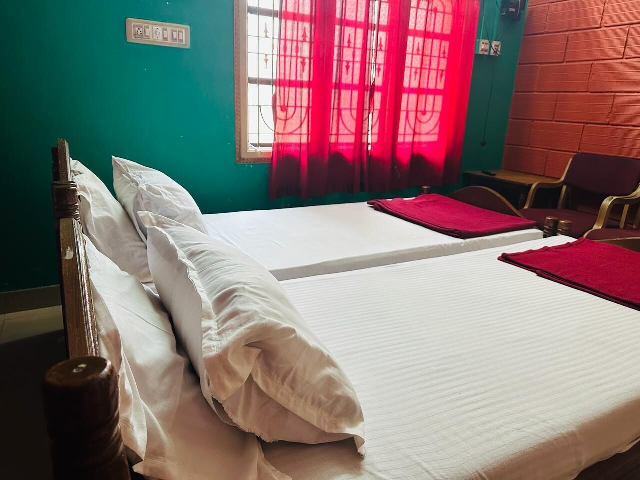 A room with two beds, a window with red curtains, a brick wall, and a wooden headboard.
