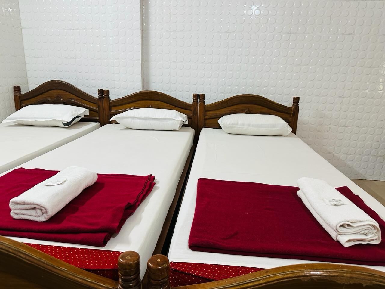 Un lit double avec une tête de lit en bois, du linge de lit blanc et des serviettes rouges.