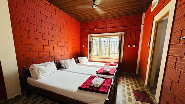 A room with two beds, a wooden ceiling, red brick walls, and a patterned floor. - Shree Katyayani Residency (Gokarna)