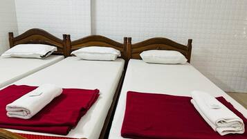 Een tweepersoonsbed met houten hoofdeinde, witte beddengoed en rode handdoeken.