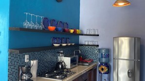 Une cuisine avec un mur bleu, des armoires en bois, un réfrigérateur en acier inoxydable, un distributeur d’eau, un four à micro-ondes, une cuisinière à gaz et un luminaire suspendu.