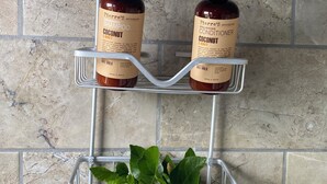 Une étagère de salle de bain avec deux bouteilles de shampoing et d’après-shampoing, et une plante en pot avec une fleur rouge.