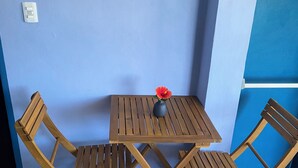 Une petite table en bois, deux chaises, un vase avec une seule fleur et un interrupteur sur le mur.