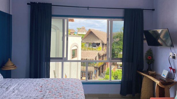Une chambre à coucher avec un lit, un bureau avec une télévision et une fenêtre avec des rideaux.