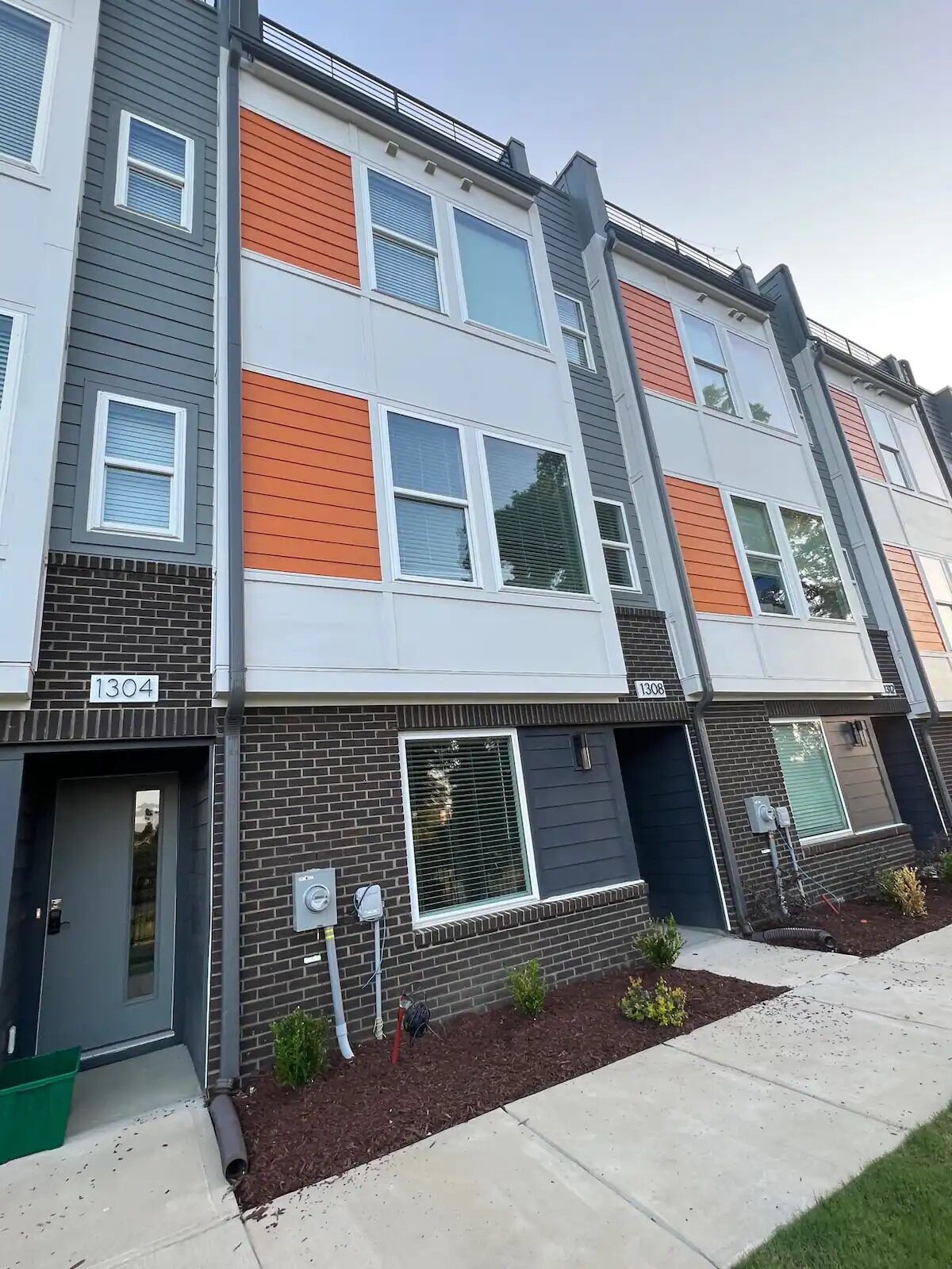 A multi-story residential building with a modern design, featuring a combination of brick and siding exteriors, and numbered units 1304 and 1308.