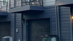 A multi-story residential building with a grey exterior, multiple windows, and a small balcony with a metal railing.