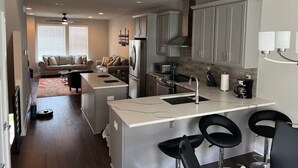 A modern kitchen with a central island, bar stools, and a dining area with a sofa and coffee table.