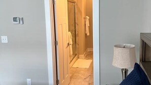 A hotel room with a bed, a nightstand, a lamp, and a view of the bathroom through an open door.