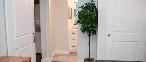 Una habitación con piso de madera, una mesita con una bandeja, una planta en maceta y una puerta blanca.