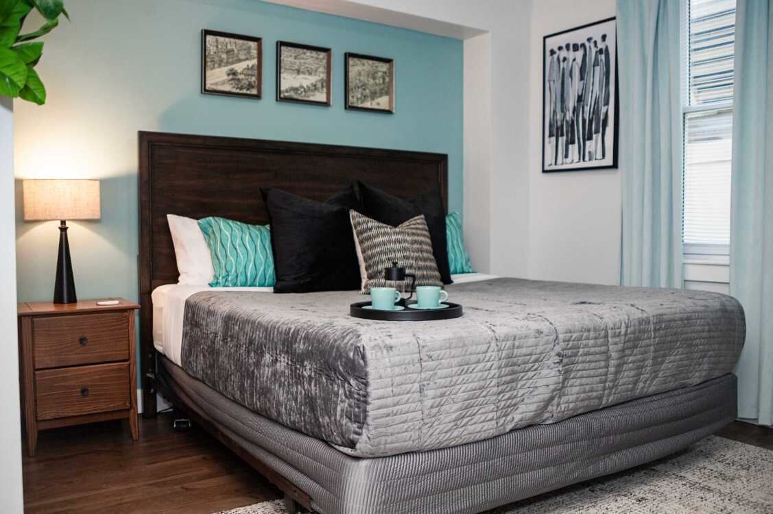 A bedroom with a large bed, a nightstand, a lamp, and artwork on the walls.