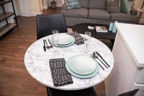Una mesa de comedor con platos, cubiertos y vasos, con un sofá y una mesa baja al fondo.