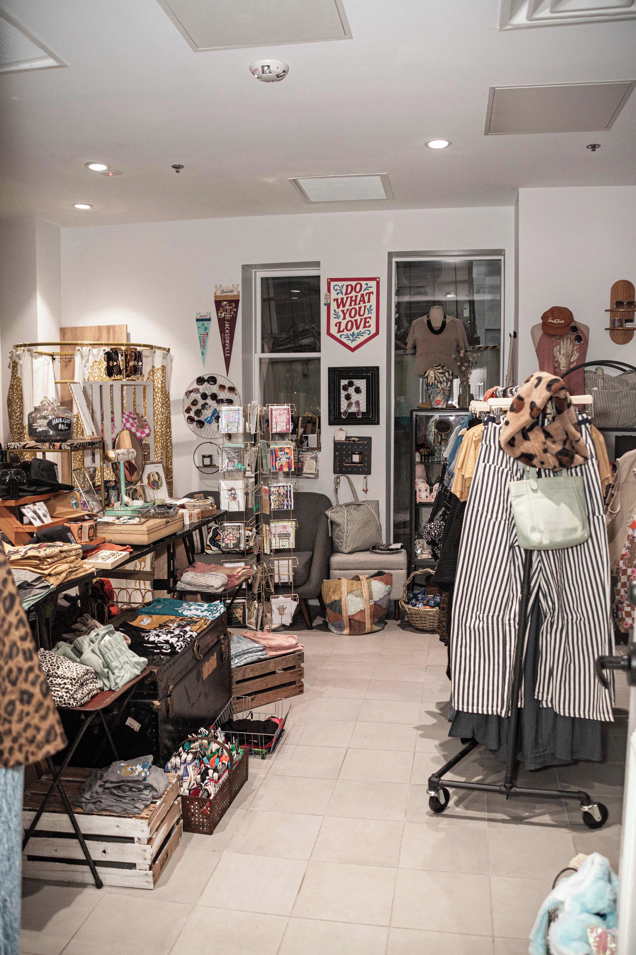 Ein Boutique-Geschäft mit verschiedenen Ausstellungsstücken, darunter Kleiderständer, Regale mit Accessoires und einer Schaufensterpuppe.