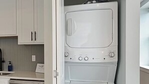A compact laundry room with a built-in washer and dryer, a stainless steel dishwasher, and white cabinetry.