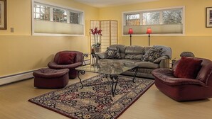 A living room with a sofa, two armchairs, a glass coffee table, and a patterned rug. - Ravens Run to the Sea - Mere Steps from the Coastal Trail: a multi use bike path (Anchorage)