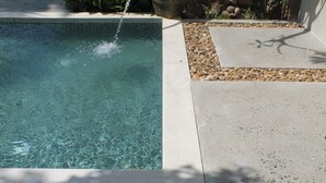 A swimming pool with clear water, surrounded by a pebble border and a concrete deck.