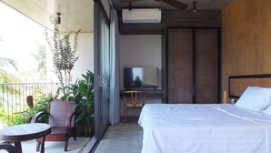 A bedroom with a bed, a television, a ceiling fan, and a balcony with plants.