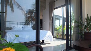 A hotel room with a bed, a view of palm trees, and a balcony with plants.
