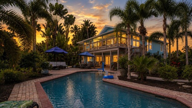 A pool with a water fountain, surrounded by palm trees and lounge chairs. - Your Hidden Florida Retreat | 4 King Suites, Luxury Kitchen, Heated Pool & Beach Adventures (Fort Myers)