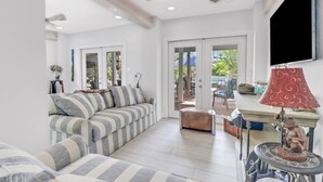 A spacious living area with a sofa, a coffee table, and a TV. There is a ceiling fan and a door leading to an outdoor patio. - Your Hidden Florida Retreat | 4 King Suites, Luxury Kitchen, Heated Pool & Beach Adventures (Fort Myers)