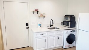 Une petite cuisine équipée d’un évier, d’un four à micro-ondes, d’un lave-linge et d’une porte.