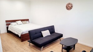 Une chambre à coucher moderne avec un lit, un canapé foncé, une petite table et une horloge murale.