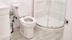 Une salle de bain moderne avec des toilettes blanches, une douche en verre et une étagère sur laquelle est posée une serviette.