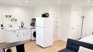 Un espace de vie compact comprenant un coin cuisine, un canapé, une table à manger et un lave-linge.