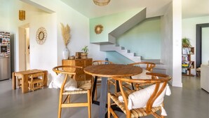 Een moderne woonkamer met een ronde houten tafel, rieten stoelen, een trap en een boekenplank.