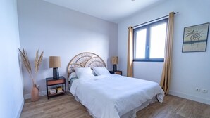 Een slaapkamer met een bed, twee nachtkastjes, een raam met gordijnen en een aan de muur hangend schilderij.